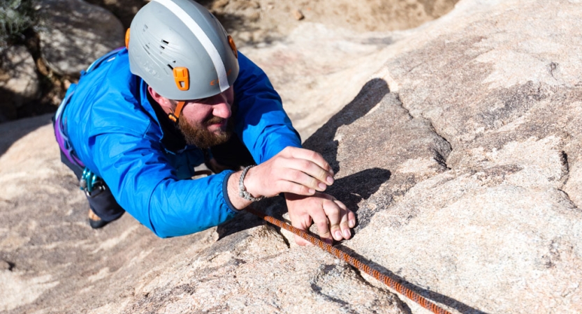 From above, a person wearing safety gear climbs towards the camera. 